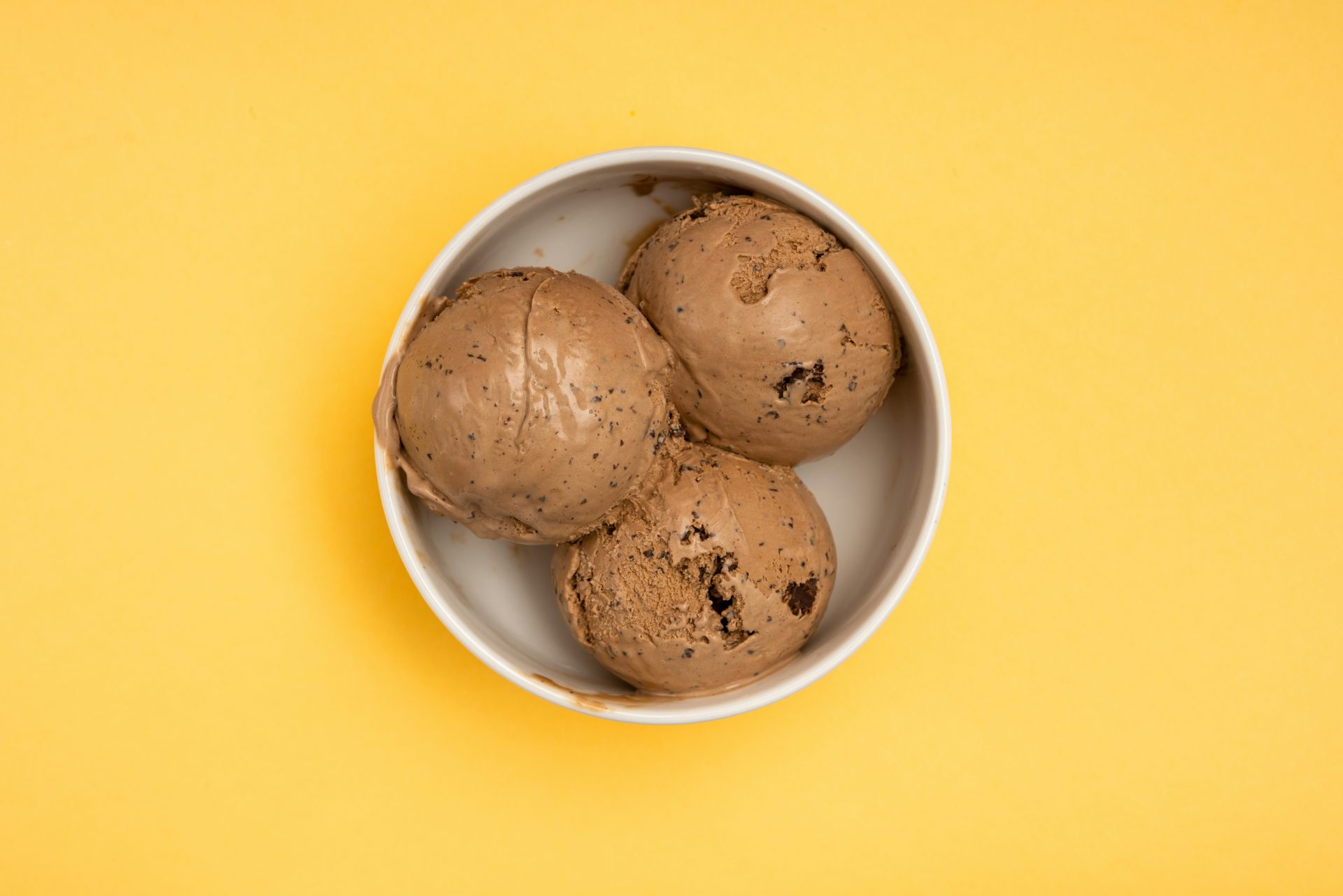 three scoops of ice cream in a bowl on a yellow background
